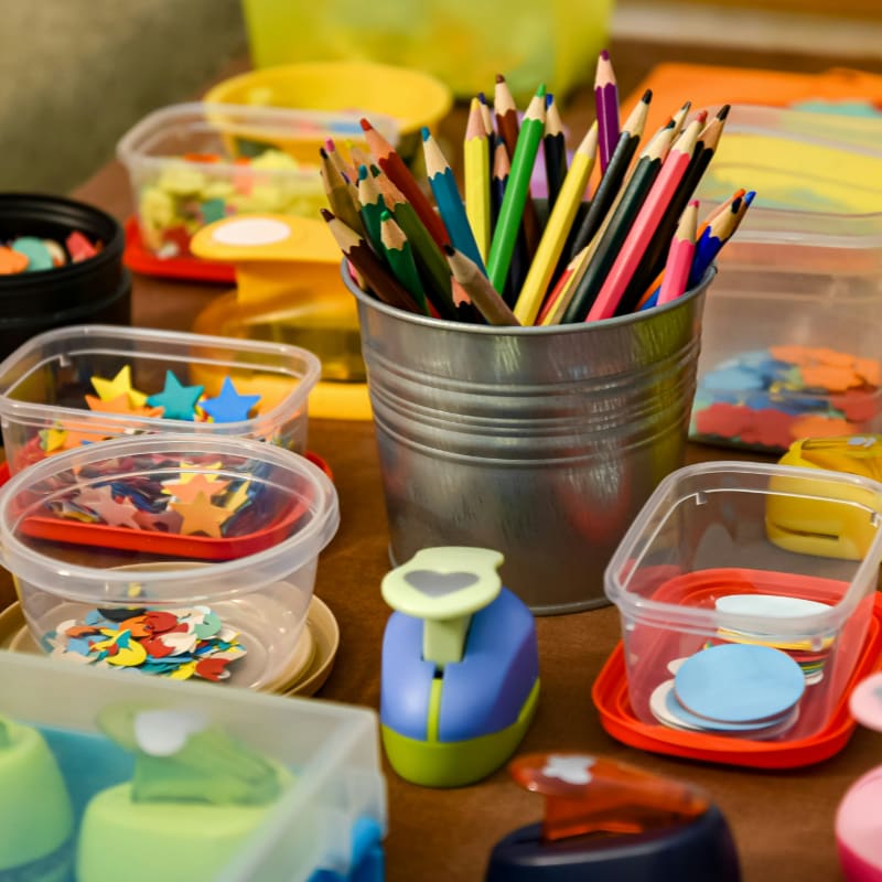 Colored pencils in a metal cup surrounded by plastic containers of paper shapes