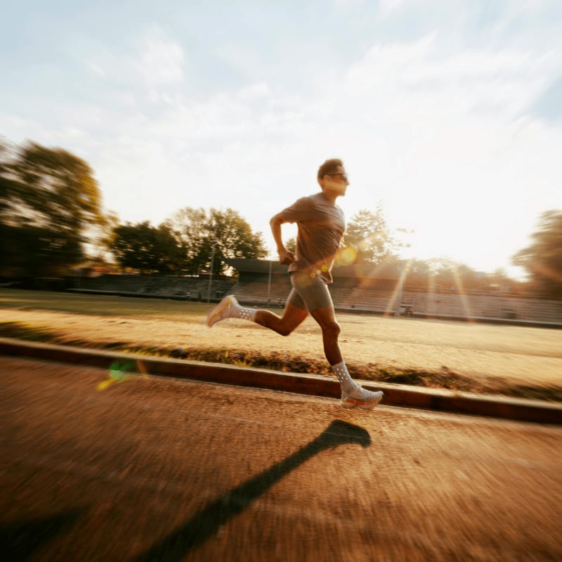 Man running on track during sunrise with lens flare