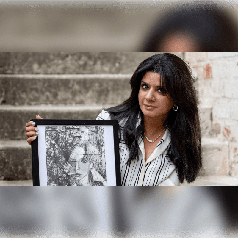 A woman in a striped pajama set sits on concrete steps with a framed picture to her right, against a brick wall.