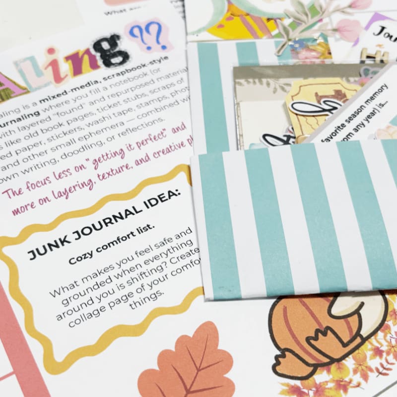 A blue and white striped card rests atop a collection of junk journal pages and decorative papers.