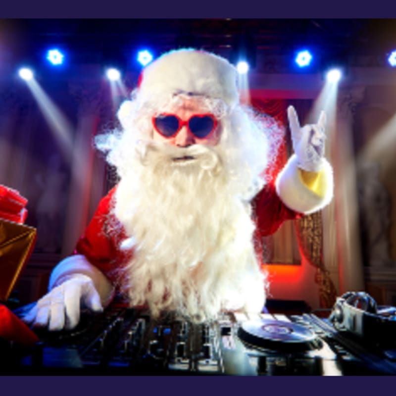 Santa Claus wearing heart-shaped sunglasses DJs at a turntable in the foreground against a background of bright blue stage lights.