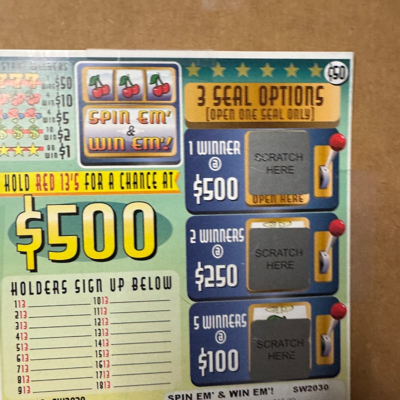 A colorful lottery-style game card with scratch-off sections and a $500 prize announcement sits against a plain brown background.