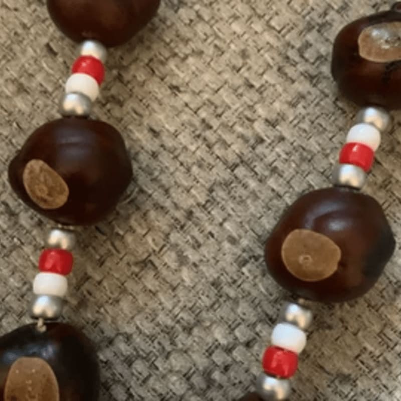Brown wooden beads separated by small red, white, and silver beads rest on a textured beige fabric background.