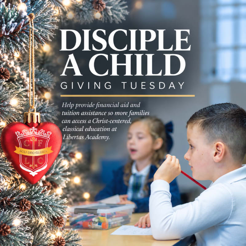 A red heart-shaped ornament hangs on a lit Christmas tree in the foreground, while a young boy and girl study at a desk in the blurred background.