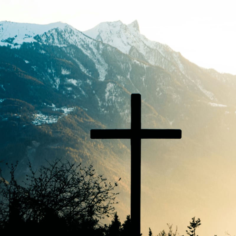A dark cross silhouette against a snow-capped mountain range in golden light
