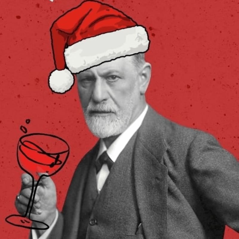 A man in a suit wearing a Santa hat and holding a glass of red wine stands against a solid red background.