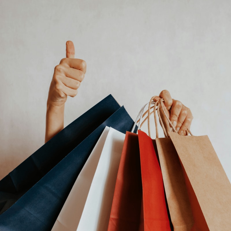 Person holding shopping bags with a thumbs up