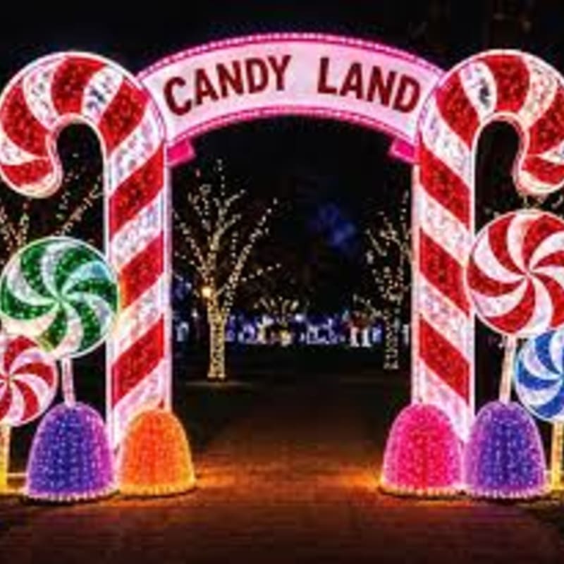 A glowing "Candy Land" archway flanked by giant candy canes and lollipops stands in the foreground, with illuminated trees sparkling in the dark background.