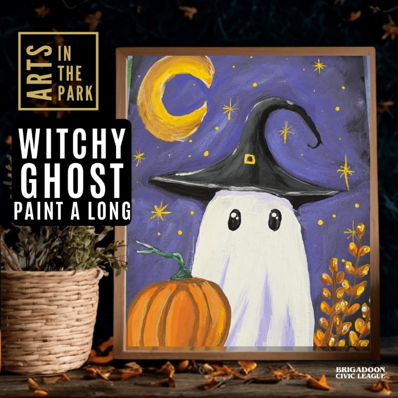A framed painting of a ghost wearing a witch's hat next to a pumpkin sits on a wooden surface beside a woven basket.