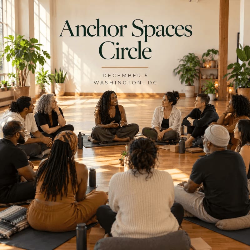 A diverse group of people sit in a circle on a wooden floor in a sunlit room filled with potted plants.