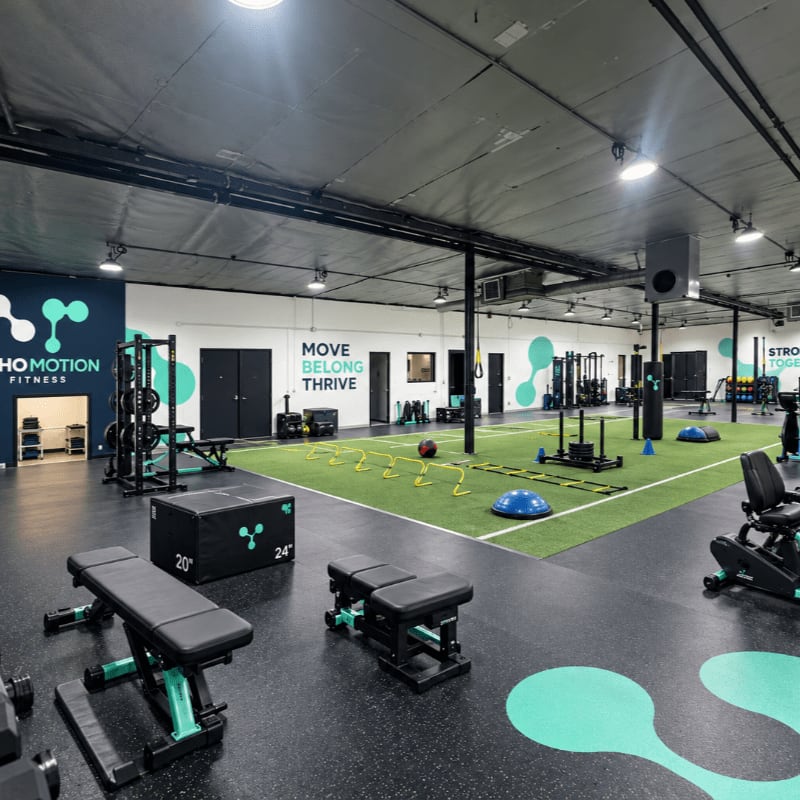 Black weight benches and a plyometric box sit in the foreground of a modern gym featuring a green turf area and various strength training equipment in the background.