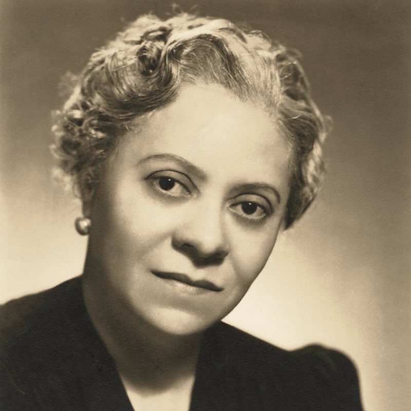 A woman with curly hair and pearl earrings is positioned in the foreground against a soft, neutral background.