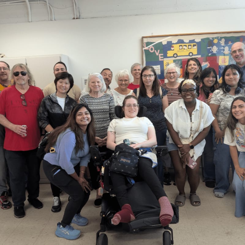 A diverse group of smiling people poses for a photo in a white room with a colorful mural on the back wall.