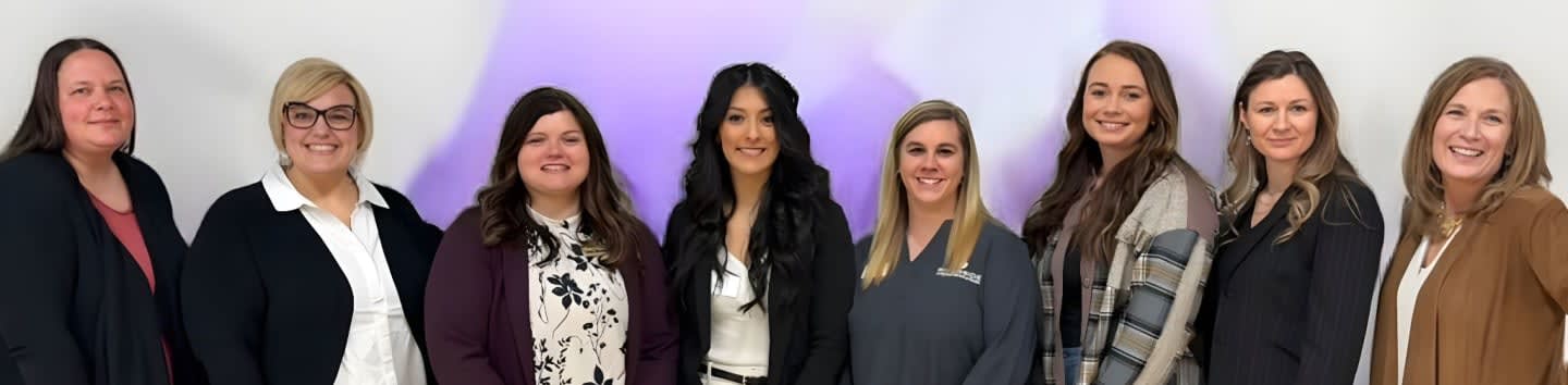 Nine women stand in a line against a white background with a purple gradient.