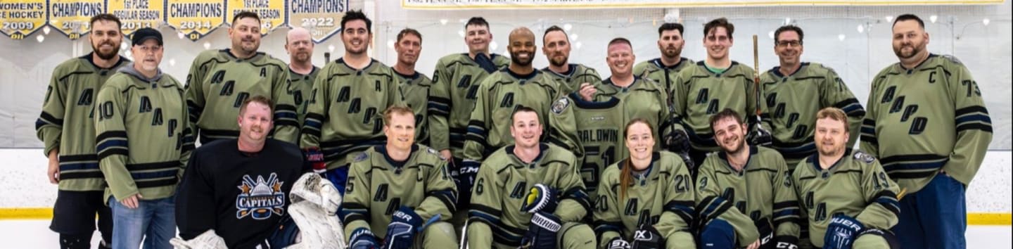 A group of hockey players in matching green jerseys pose in front of championship banners on an ice rink.