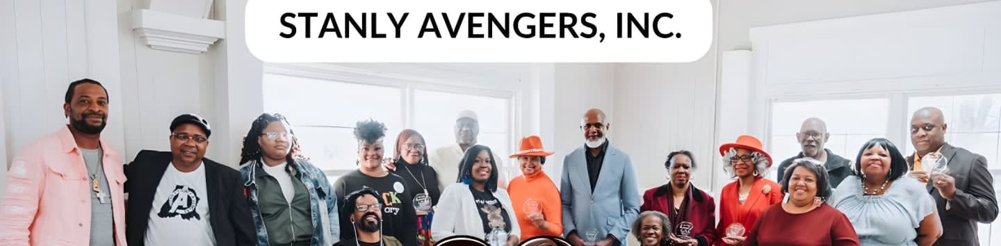 A group of people stand in front of a white wall with windows, under a banner that reads "STANLY AVENGERS, INC."