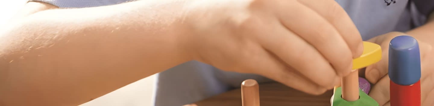 A child's hands are stacking colorful wooden blocks on a table.