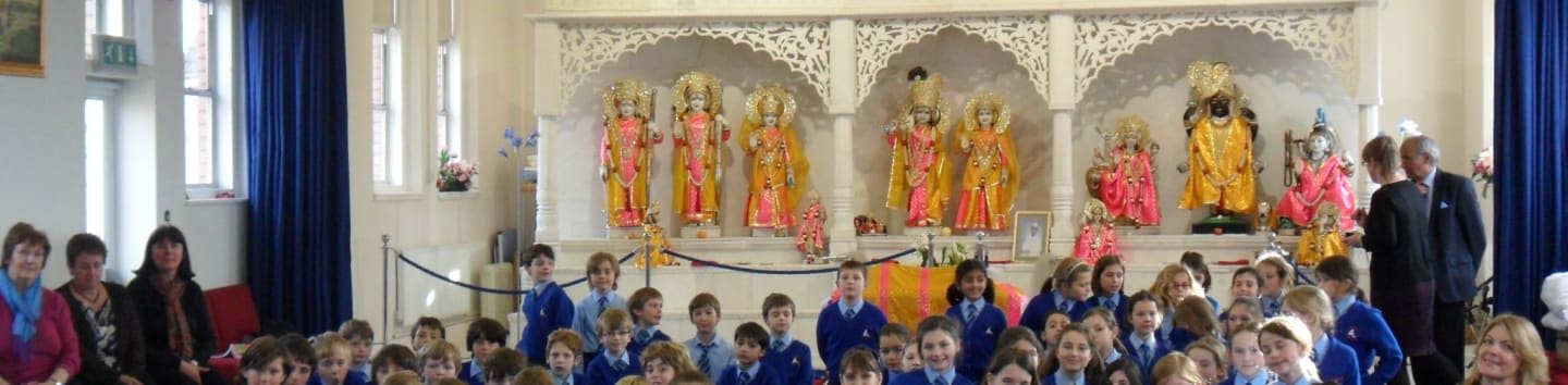 A group of children in uniform are gathered in front of a decorated altar with statues of deities, while adults stand to the side.