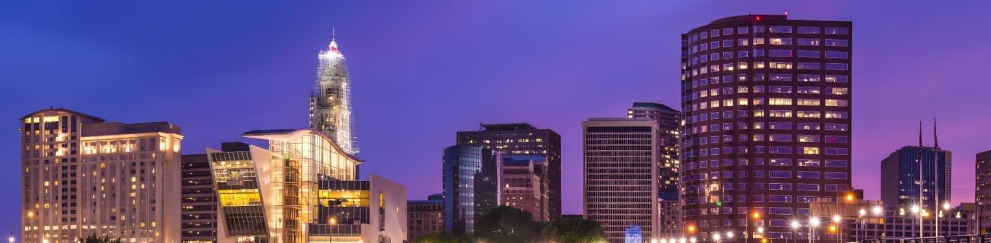Illuminated skyscrapers stand against a twilight sky, with a blurred cityscape in the foreground.