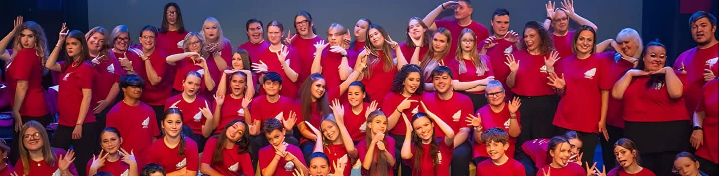 A large group of people in red shirts pose for a photo in front of a dark background.