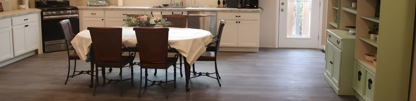 A dining table with chairs is set in the foreground, while a kitchen and a light green cabinet are in the background.