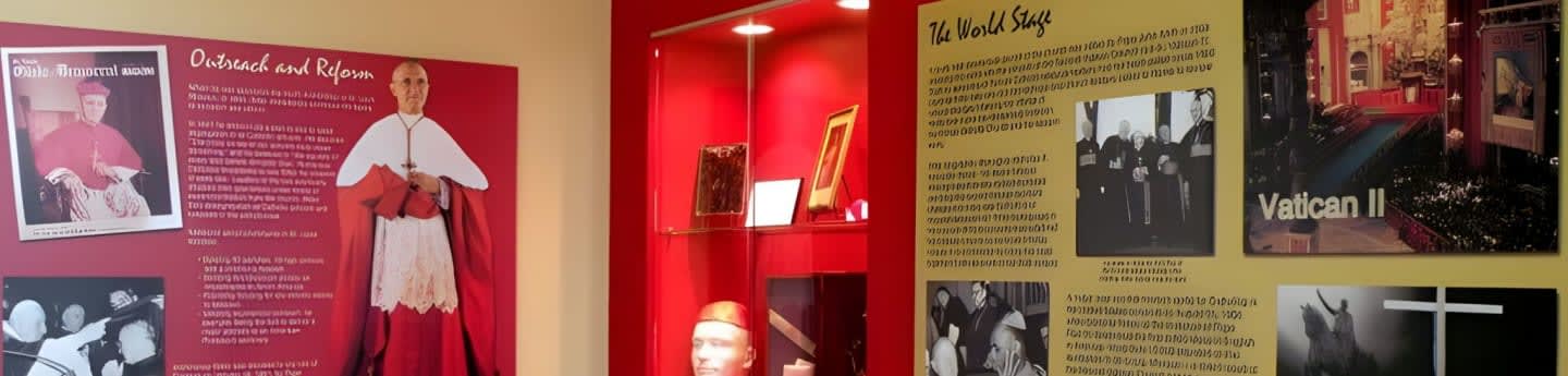 A display features a mannequin dressed as a cardinal in the foreground, with informational panels and historical photographs about Vatican II in the background.