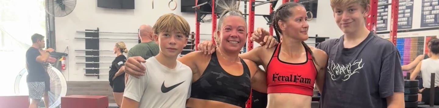 Four people pose for a photo in a gym with weight racks and equipment in the background.