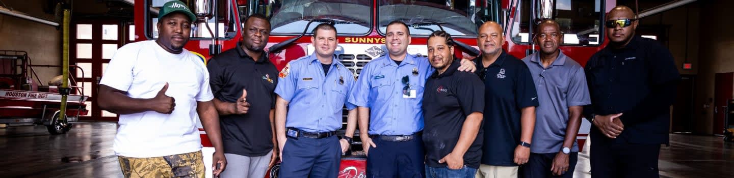 A group of men stand in front of a fire truck in a fire station.