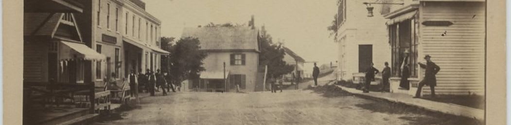 A street scene with people and buildings lines the foreground, while a hazy sky and distant structures form the background.