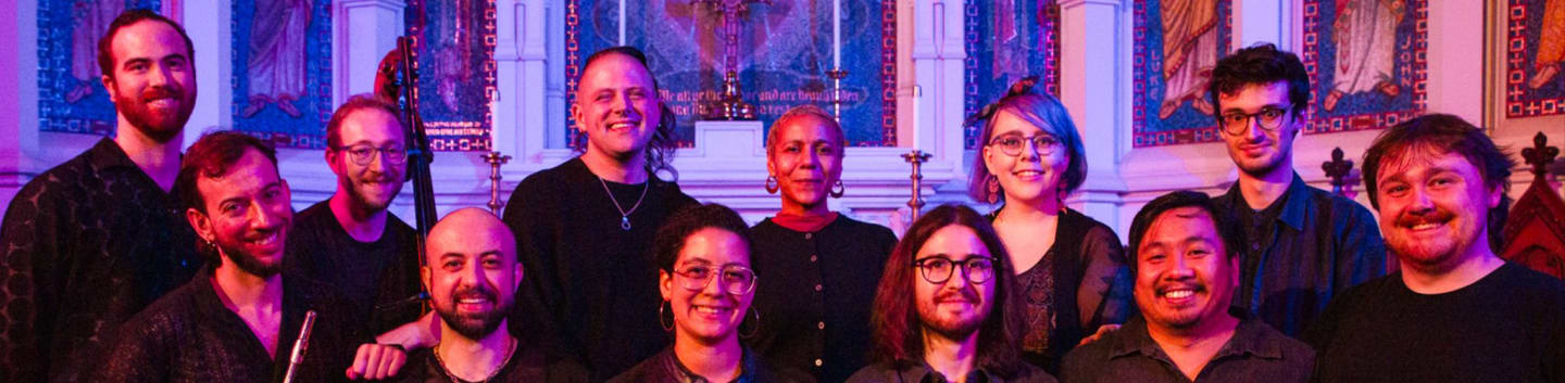 A diverse group of people smile at the camera in front of a dimly lit, ornate church interior.
