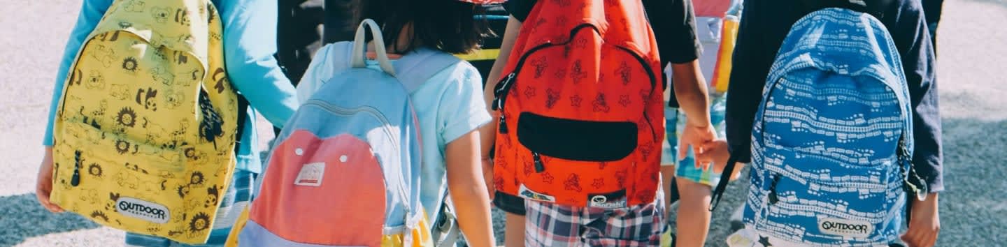 group of people wearing white and orange backpacks walking on gray concrete pavement during daytime