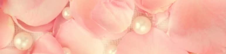 Soft pink rose petals are scattered with luminous pearls in the foreground, against a blurred, dreamy background of more petals.