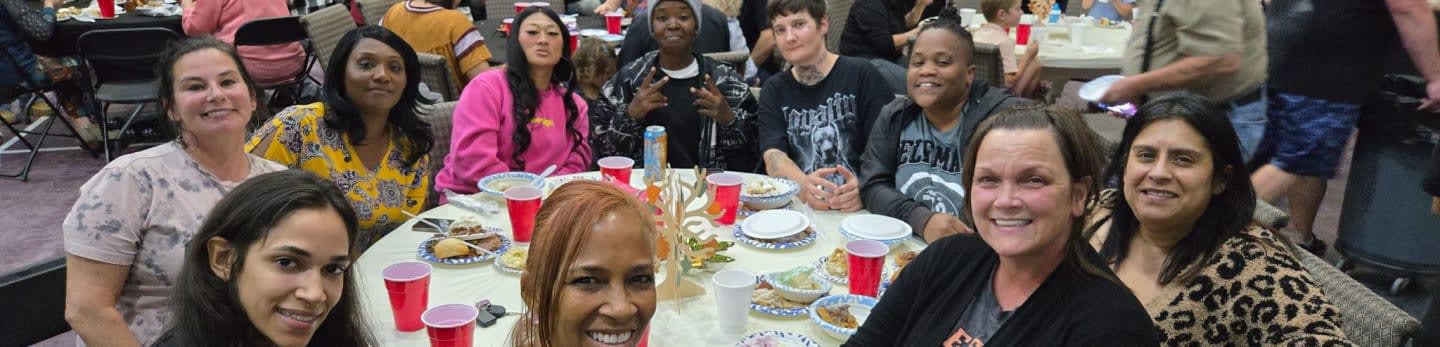 A group of people are gathered around a table with red cups and plates of food, while others stand in the background.