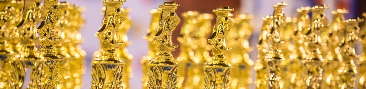 Rows of golden trophies gleam in the foreground, with a blurred, colorful background.