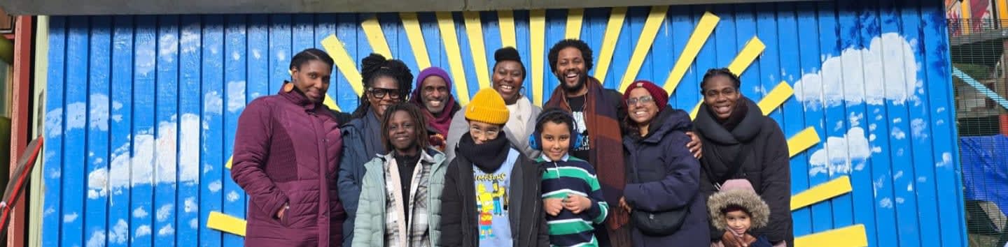 A group of people stand in front of a vibrant blue mural featuring yellow sun rays and white clouds.