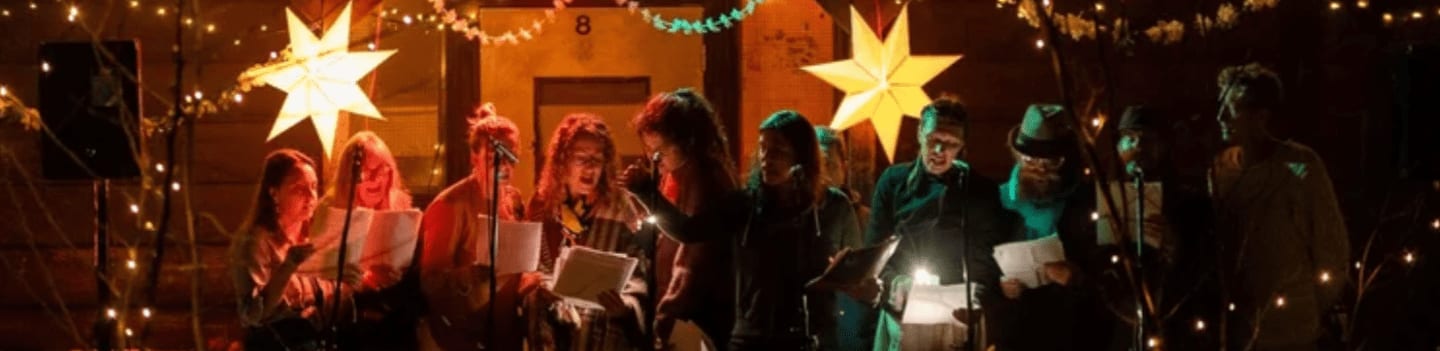 A group of people are singing in front of a building decorated with Christmas lights and stars.