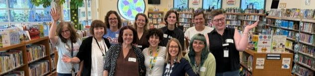 A group of smiling people stand in front of bookshelves filled with books in a library.