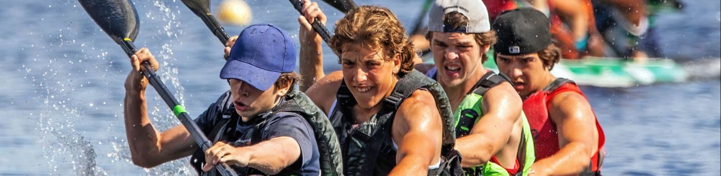 Four determined people paddle a boat through splashing water with other racers blurred in the background.