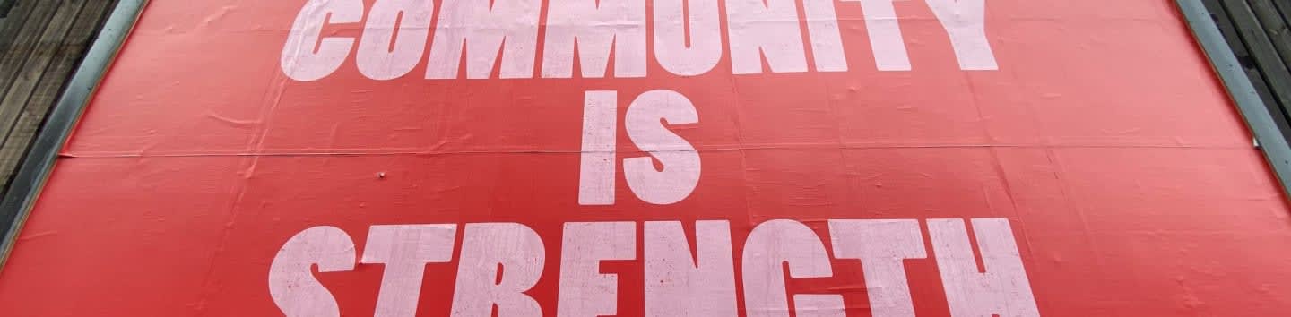 A large red billboard with white text reading COMMUNITY IS STRENGTH on a building