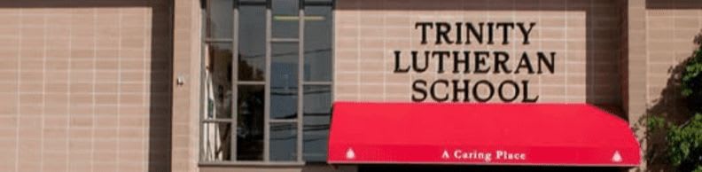 A red awning shades the entrance to Trinity Lutheran School, with a crosswalk in the foreground and a clear blue sky in the background.