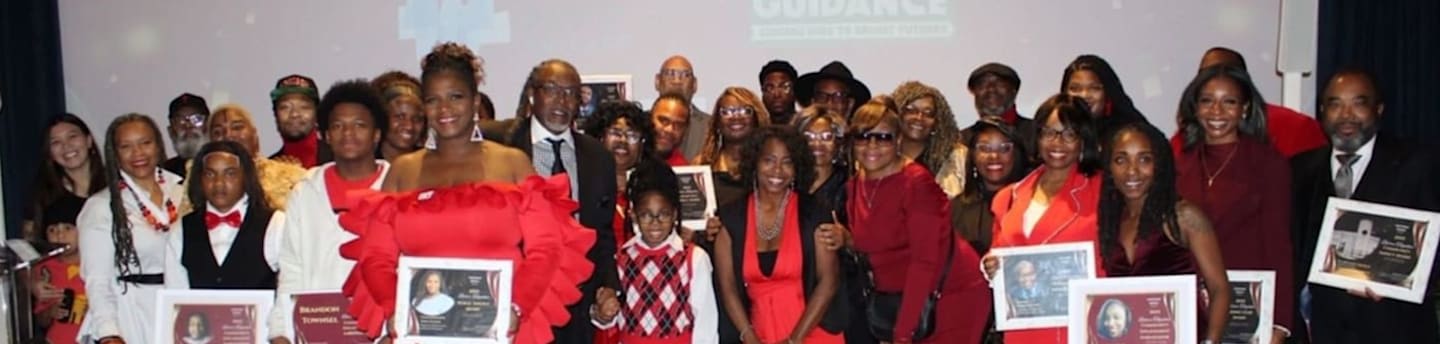 A large group of people dressed in red, white, and black attire pose for a photo in the foreground against a light-colored backdrop.