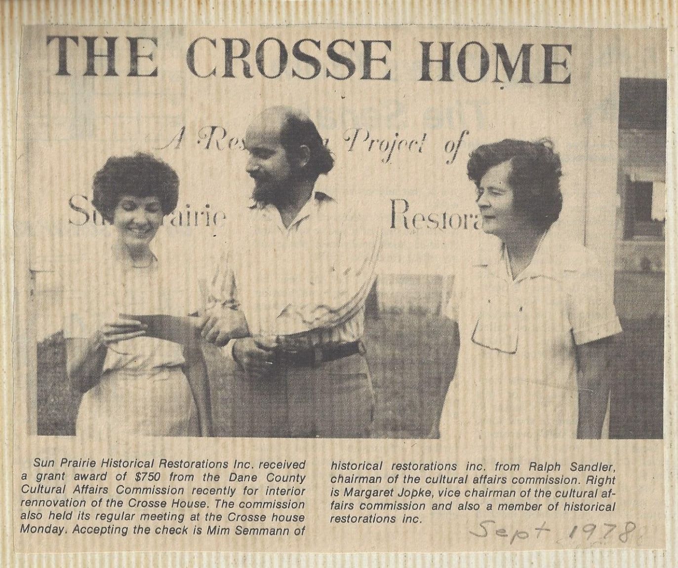 Three people stand in front of a banner that reads "THE CROSSE HOME," with two women and a man in the foreground.
