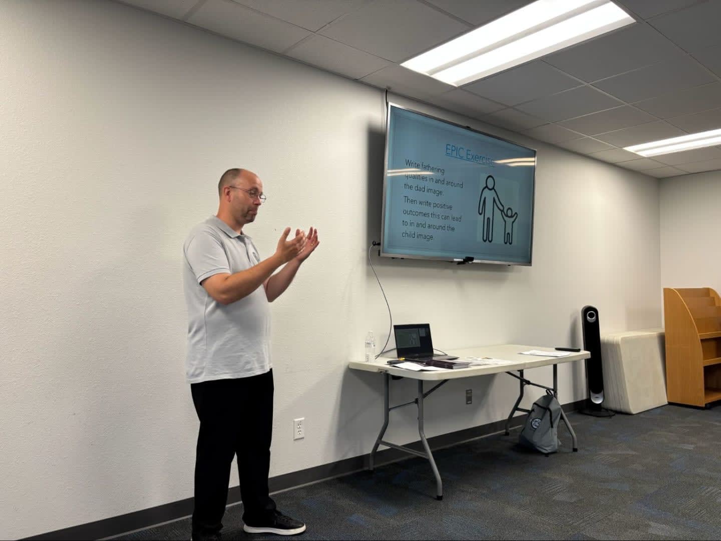 A man gestures with his hands in the foreground while a presentation about child safety is displayed on a large screen in the background.