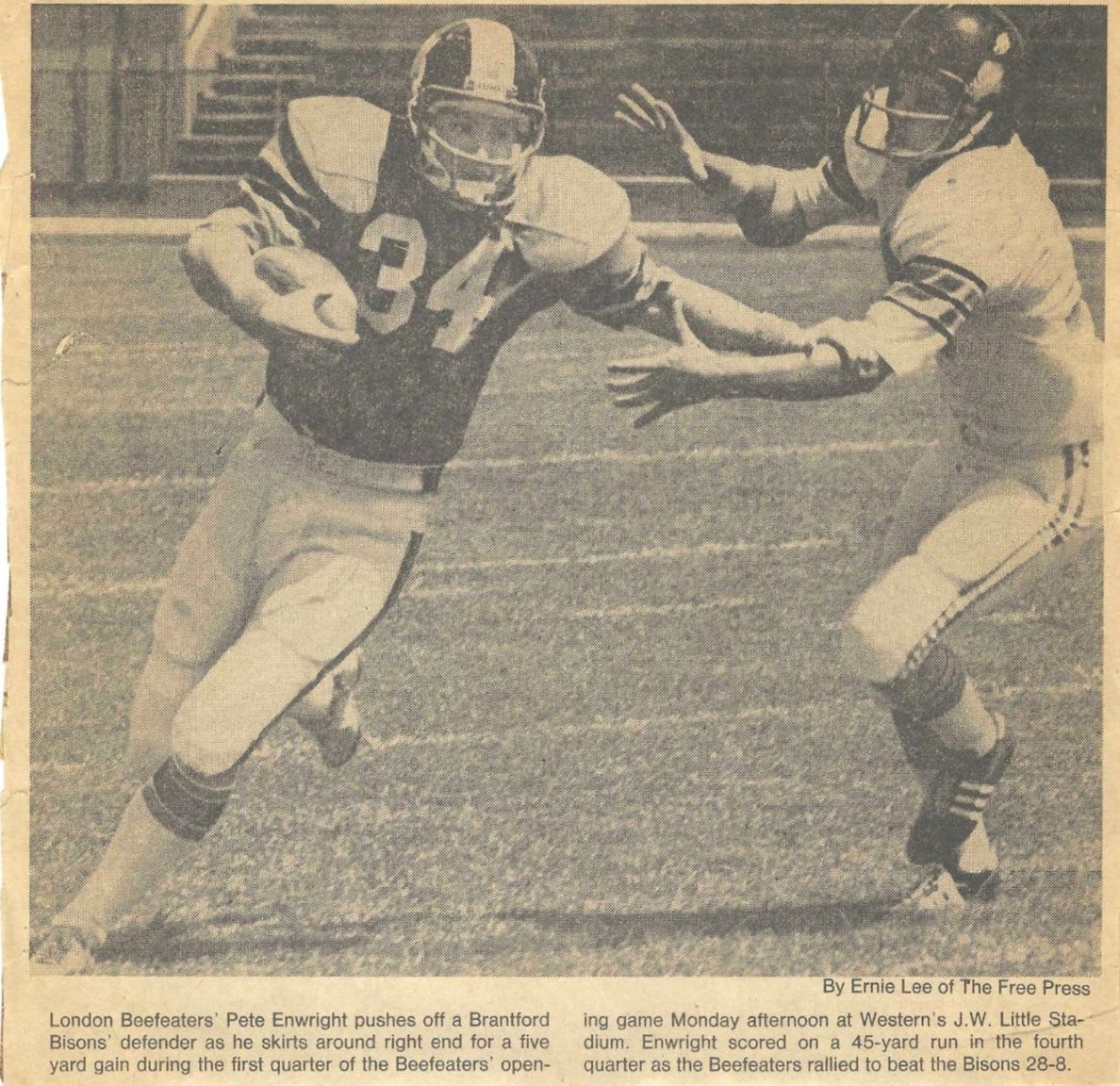 A football player in a yellow and blue uniform with the number 34 on his jersey runs with the ball, pursued by a defender in a yellow and black uniform, with a stadium and bleachers visible in the background.