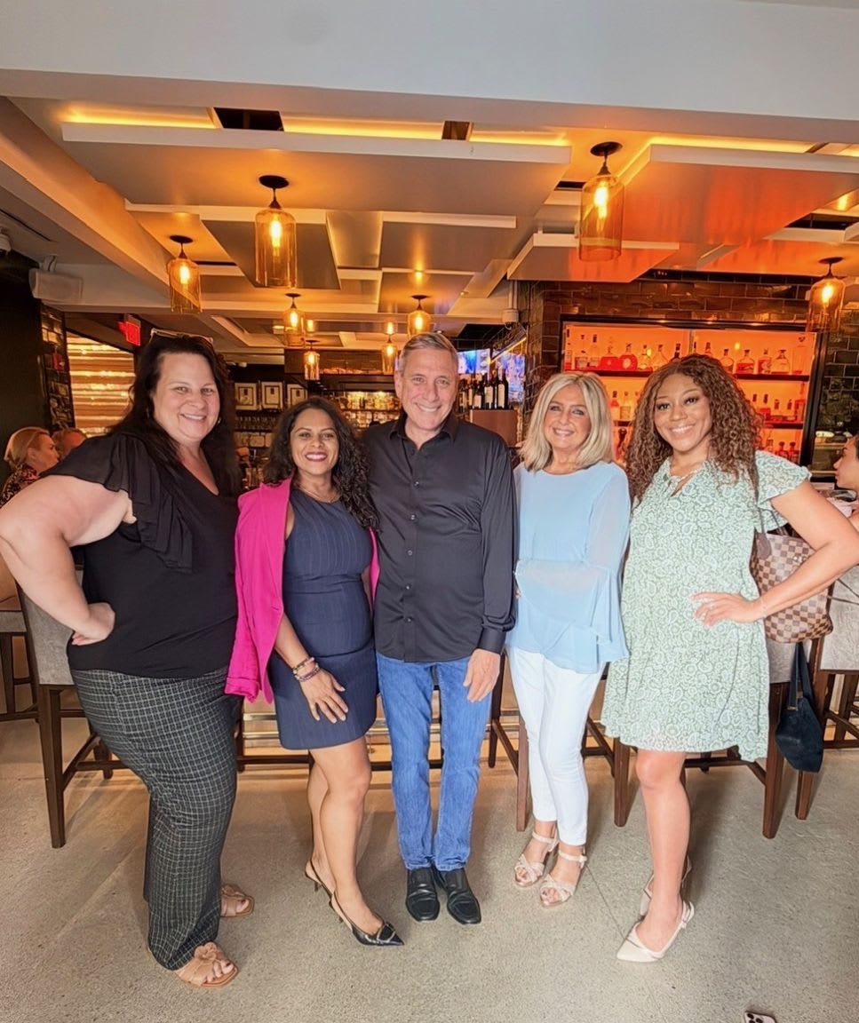 Five people pose for a photo in a restaurant with a bar and decorative lighting in the background.
