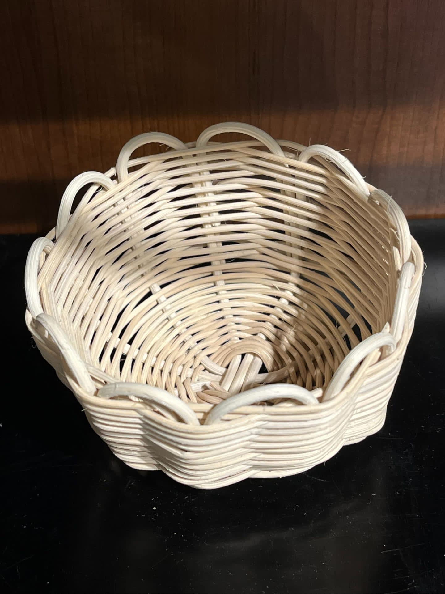A light-colored woven basket with a scalloped rim sits on a dark surface in front of a wooden background.