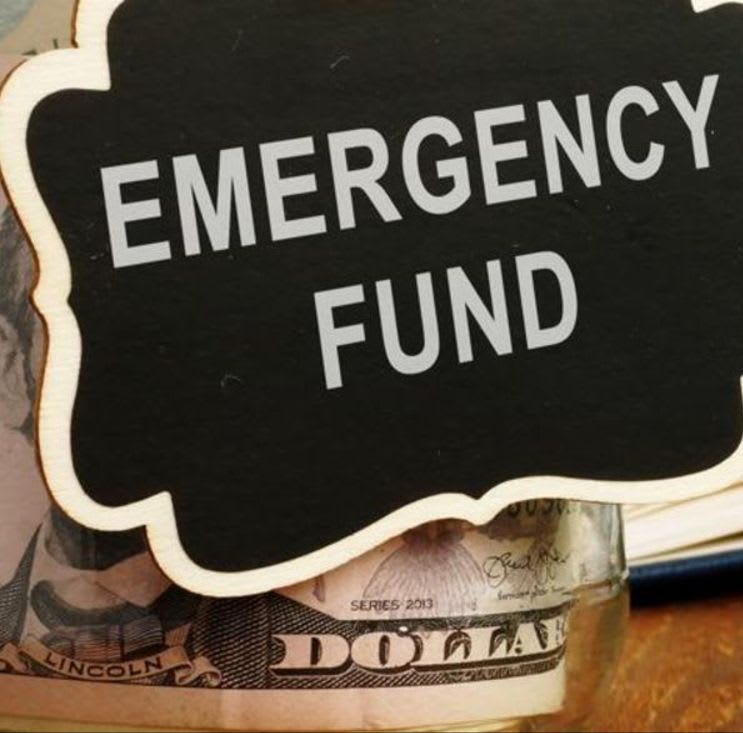 A chalkboard sign reading "EMERGENCY FUND" rests on a jar filled with dollar bills.