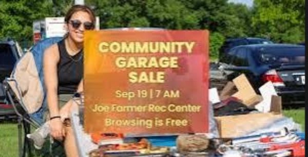 A young woman sits in a chair next to a "Community Garage Sale" sign, with various items for sale piled in front of it and cars parked in the background.