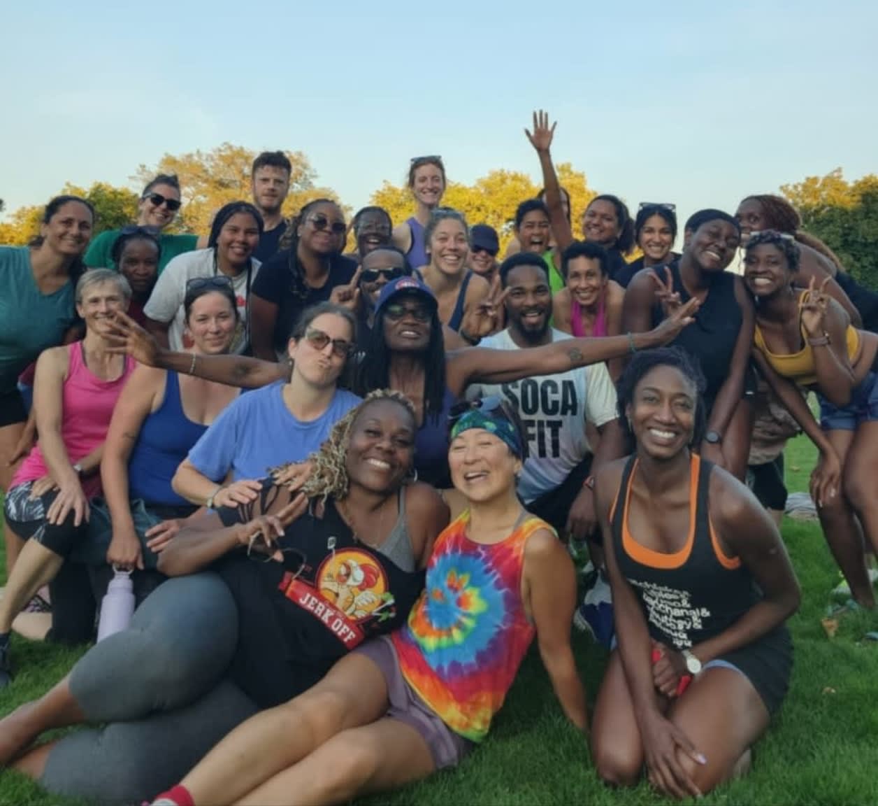 A diverse group of people in athletic wear pose for a photo on a grassy field with a clear sky in the background.