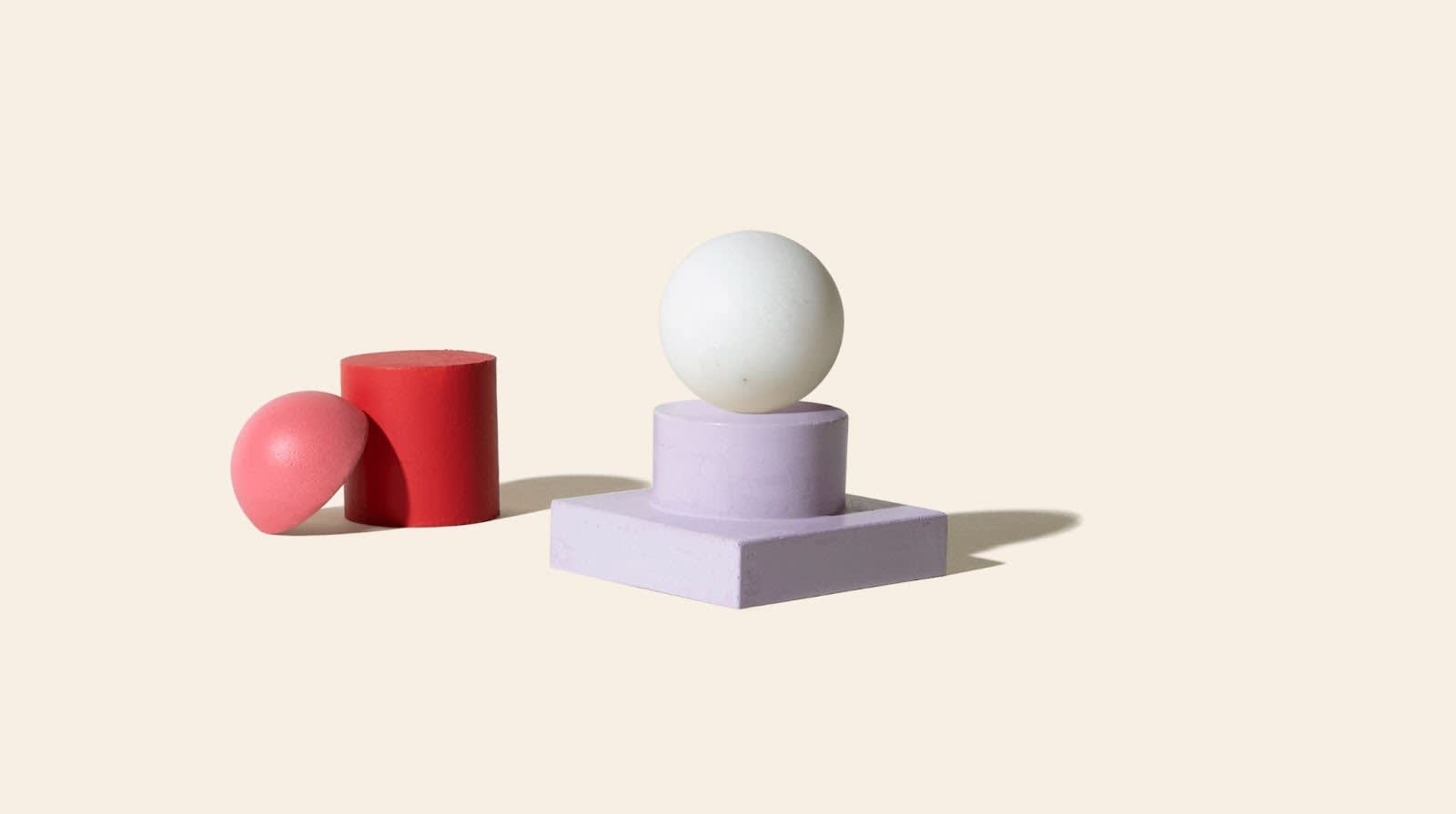 3D marble ball sitting on top of a purple stone pedestal at the center of a beige background. A red 3D cylinder sits to the left of the pedestal. A halved pink marble ball leans on the cylinder. All of the images cast small shadows.